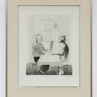 A framed etching by David Hockney, the artwork shows an artist and model seated across from each other at a table inside a private setting. The artist is wearing a striped shirt and dark pants and is holding a piece of paper in front of him. The model is a male figure with glasses, and is naked and sitting on a cushioned seat.